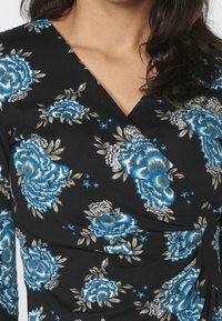 Blumenkleid mit blauen Rosen und silbernen Akzenten auf einem schwarzen Stoffhintergrund; strukturiertes Material mit Raffung.