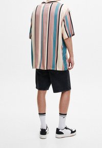 Camicetta a maniche corte a righe multicolori in tonalità pastello, abbinata a pantaloni corti in denim scuro. Calze bianche e scarpe da ginnastica nere e bianche completano l'outfit.