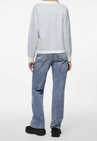 Biało-niebieski sweter w paski z ribbowymi mankietami, zestawiony z jasnoniebieskimi prostymi dżinsami i czarnymi masywnymi trampkami.