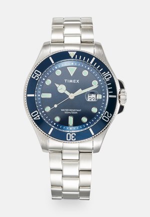Timex-Uhr mit einem Armband aus rostfreiem Stahl. Das dunkelblaue Zifferblatt verfügt über leuchtende Indizes und Zeiger, ist bis 100 m wasserdicht und hat ein Datumsfenster bei 3 Uhr.