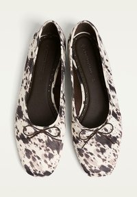 Ein Paar schwarz-weiße gepunktete Ballerinas mit abgerundeten quadratischen Zehen und kleinen dekorativen Schleifen auf einem hellen Hintergrund.