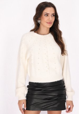 Pull en maille texturée de couleur crème avec des accents en perles et des bords côtelés, associé à une mini jupe en cuir noir plissée.