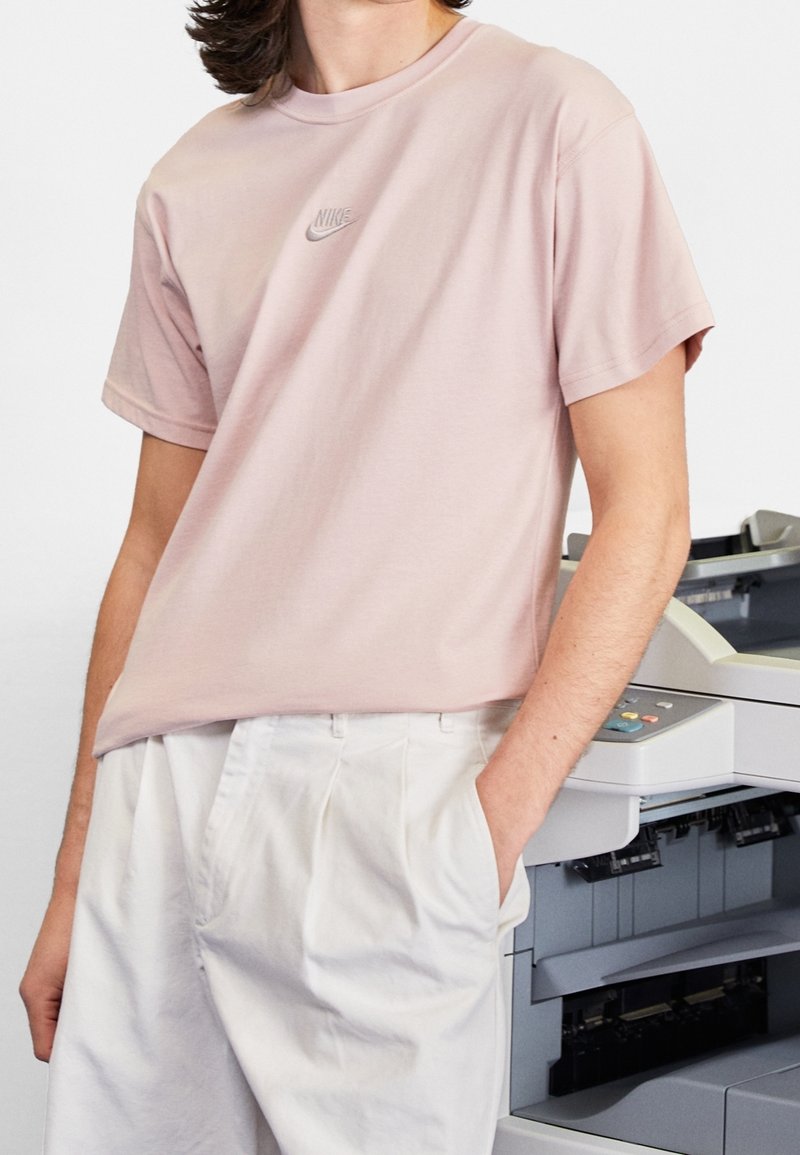 Ljusrosa bomulls t-shirt med rund hals och korta ärmar, med en liten grå Nike-logotyp på bröstet. Avslappnad passform.
