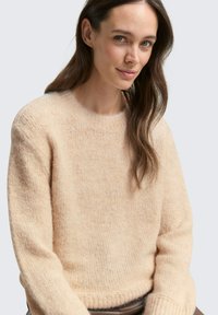 Hellpfirsichfarbener, gestrickter Pullover mit Rundhalsausschnitt, gerippten Bündchen und einer weichen, strukturierten Oberfläche. Hat eine lockere Passform und ein einfaches Design.
