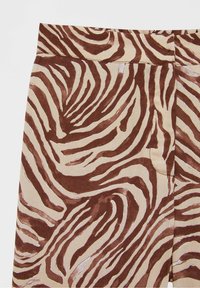Gros plan sur un tissu à motif animal en marron et beige avec un motif de rayures ondulées, montrant les détails de la taille et de la couture.