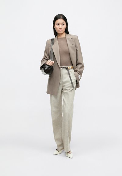 Μπεζ σακάκι πάνω από ένα καφέ εφαρμοστό τοπ, ανοιχτό γκρι παντελόνι και κρεμ μυτερές γόβες. Τα αξεσουάρ περιλαμβάνουν μια στρογγυλή μαύρη τσάντα με υφή.