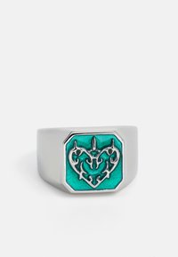 Srebrni prsten sa kvadratnom teal emajliranom površinom koja sadrži ornamenatski dizajn srca s centralnim šiljastim detaljem.
