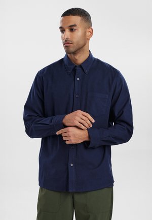 Dunkelblauses Button-Up-Hemd aus einem weichen Stoff. Verfügt über eine Brusttasche, einen Kragen und lange Ärmel. Mit subtiler Textur und lässigem Schnitt.