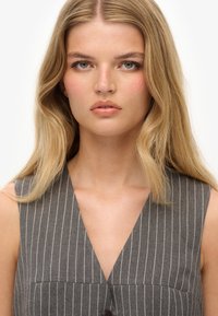 Szary, w paski bezrękawnik z dekoltem w kształcie litery V i guzikiem z przodu, wykonany z gładkiego materiału o subtelnej fakturze.