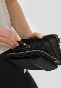 Portafoglio in pelle nera con finitura testurizzata, zip dorata e molteplici scomparti. Presenta una piccola tracolla per una facile gestione.