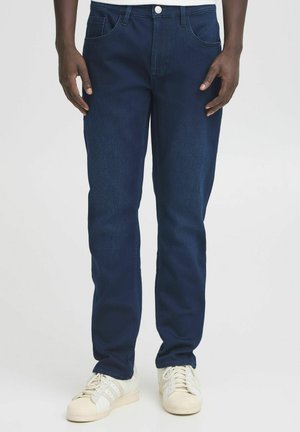 Mørkeblå denimjeans med rette ben, fem-lommers design, knappelukking og en glatt tekstur. Kombinert med hvite joggesko.