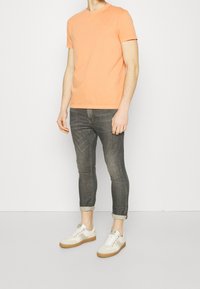 Camiseta melocotón con cuello redondo, combinada con vaqueros ajustados de denim gris y zapatillas blancas con suela marrón.