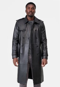 Black leather trench coat with double-breasted buttons, epaulets on shoulders, and side pockets. Smooth texture and knee-length design.