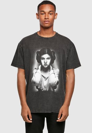 Ung mand iført en falmet sort T-shirt med et gråtonet portræt af en kvinde med stylet hår og hænder nær hendes hals.
