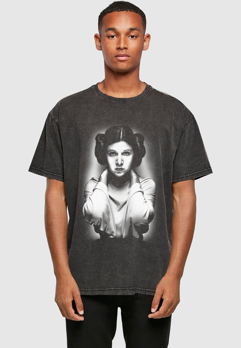 Jeune homme portant un t-shirt noir délavé avec un portrait en niveaux de gris d'une femme aux cheveux coiffés et les mains près de son cou.