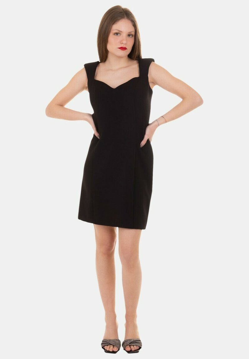 Abito nero con scollatura quadrata e maniche a dolcevita, caratterizzato da una silhouette aderente e una texture liscia. Indossato con scarpe nere open-toe.