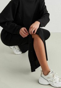 Sort langærmet kjole med knapdetaljer på siden, parret med hvide og grå sneakers. Blødt stof og afslappet pasform.