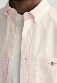 Camisa de cuadros en rosa claro de tela de algodón, con cuello tipo polo, bolsillo en el pecho con logo bordado y una textura sutil.