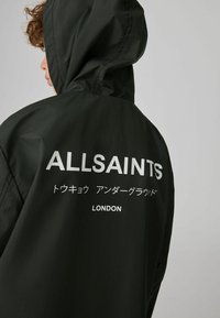 Sort hættetrøje med vertikal linjetekstur, stort hvidt "ALLSAINTS"-logo og yderligere tekst på japansk samt "LONDON" bagpå.