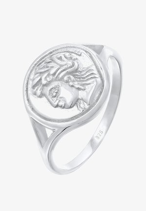 Silver ring with a round, raised emblem featuring a detailed face, smooth finish, and cutout accents on the band. Marked 925 inside.