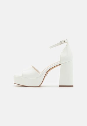 Sandales à plateforme blanches avec un bout arrondi, un épais talon bloc et une bride à la cheville. Fabriquées en matériau vernissé lisse avec un design minimaliste.