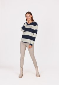 Maglietta a maniche lunghe a righe in grigio chiaro e blu navy con dettaglio della tasca. Abbinata a pantaloni beige aderenti e stivaletti alla caviglia color taupe. Texture liscia.