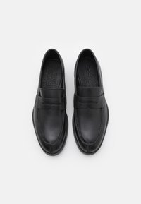 Melni ādas loafers ar gludu apdari, ar šūtu dizainu, noapaļotu pirkstu un dekoratīvu joslu augšpusē. Strukturēta iekšzole.