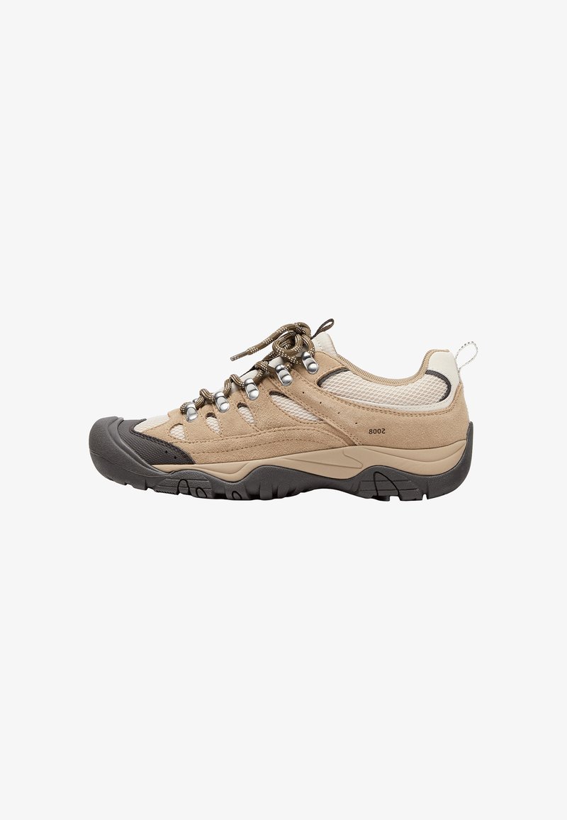 Chaussure de randonnée beige et marron clair avec semelle extérieure noire, œillets métalliques, panneaux en mesh et lacets épais et ronds sur fond blanc.