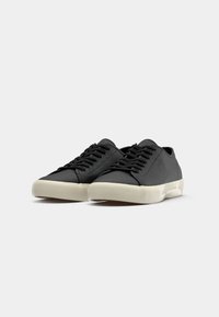 Pair of black low-top sneakers with beige textured rubber soles and black laces, displayed against a plain white background.