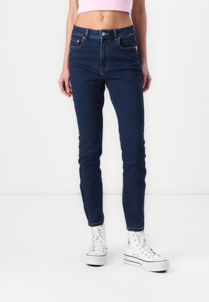 Smarte skinny jeans laget av mørk denim, med høy midje, to frontlommer og subtile sømdetaljer, kombinert med hvite sneakers.