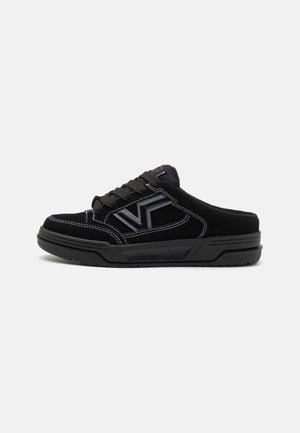 Baskets slip-on noires avec lacets, coutures blanches visibles, semelle épaisse et logo "VF" sur le côté, montrées de profil sur un fonds clair.