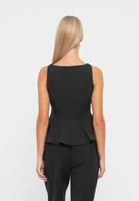 Sort peplum-top med rund halsudskæring og sømdetaljer, lavet af tekstureret stof. Stylet med matchende sorte bukser.