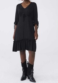 Svart klänning med V-ringning, trekvarts ärmar och dragsko i midjan. Har en volangnederdel och mjukt material. Bärs med svarta cowboykängor.