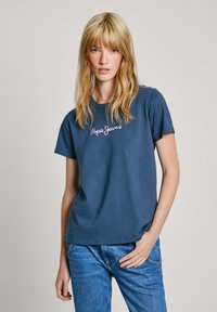 Tamsiai mėlynos spalvos medvilninė marškinėliai trumpomis rankovėmis, apvaliu iškirpimu ir "Pepe Jeans" siuvinėjimu balta ir raudona spalva priekyje. Atsitiktinė prigludusi forma.