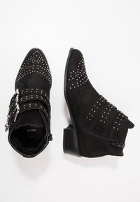 Botas de tobillo de ante negro con punteras afiladas, adornos con tachuelas, correas con hebillas y cremalleras laterales. Tacones de bloque bajos.