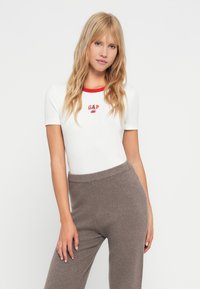 Haut blanc à manches courtes avec un col côtelé rouge et un logo "GAP" brodé. Associe-le à un pantalon en tricot gris avec une taille côtelée.
