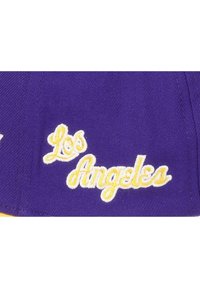 Gorra de béisbol morada con texto amarillo bordado que dice "Los Ángeles". Cuenta con una corona estructurada y un borde curvado.