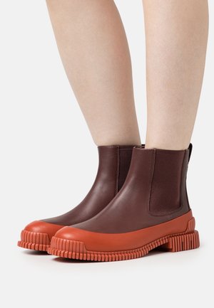 Bottines marron imperméables avec des panneaux latéraux en élasthanne et une semelle en caoutchouc orange texturée, présentant un design strié et un bout rond.