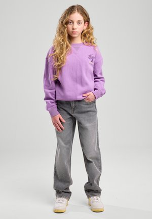 Felpa viola con scollatura tonda e design ricamato, abbinata a jeans grigi e sneakers bianche con accenti gialli.