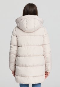 Kurtka puchowa w jasnym beżu z kapturem, z poziomymi przeszyciami i gładką, błyszczącą fakturą. Stylizowana w luźnym kroju.