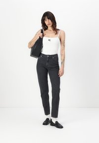 Melni augstās jostasvietas džinsi, balts ribots topiņš ar nelielu grafiku un melna plecu soma. Melni apavi ar baltām zeķēm pilnveido izskatu.