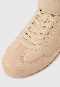 Baskets beiges combinant cuir lisse et daim doux, avec des lacets plats, un embout renforcé et une sangle de cheville rembourrée.