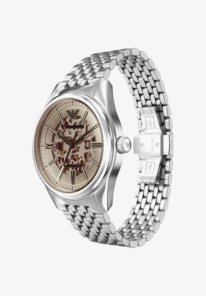 Orologio in acciaio inossidabile con cinturino a maglia argentato, quadrante scheletrato beige, numeri romani e cassa lucida. Presenta un logo inciso sul lato.