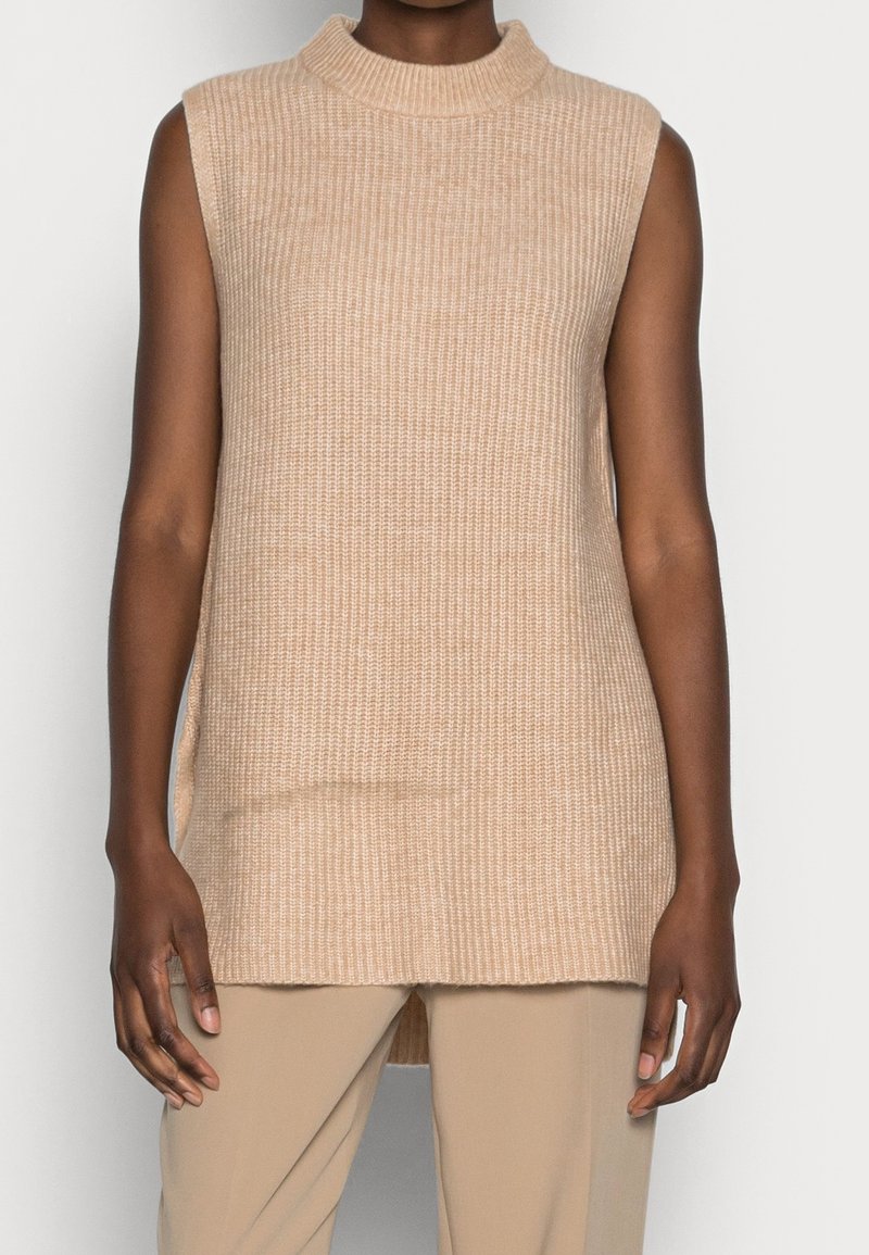 Débardeur en maille sans manches de couleur beige clair avec un col haut, doté d'une texture côtelée et de fentes latérales pour faciliter les mouvements.