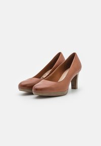 Chaussures à talons en cuir marron avec un bout arrondi, un talon à texture bois et une surface lisse. Le design présente un style classique de compensé.