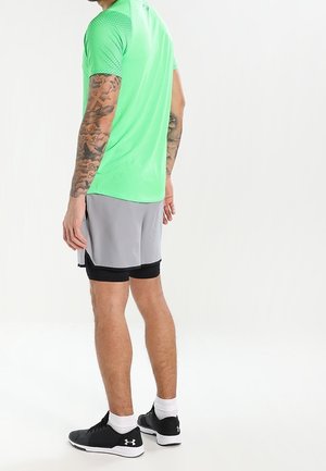 T-shirt de sport à manches courtes vert fluo avec des panneaux en mesh sur les épaules, accompagné de shorts gris et de chaussures de sport noires.