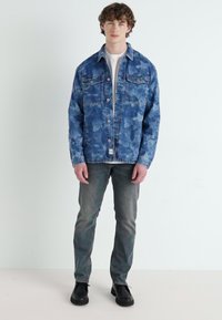 Denim jakna svijetloplave boje s izbljeđenim uzorkom, dva džepa na prsima, kopčanje na gumbi i sivi traperice. Crne cipele upotpunjuju odijelo.