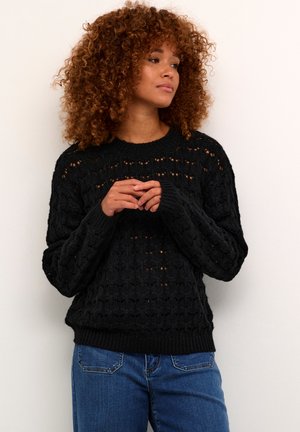 Maglione nero a maglia con motivo traforato, collo e polsini a costine e vestibilità ampia. Abbinato a jeans blu, mette in evidenza uno stile casual.