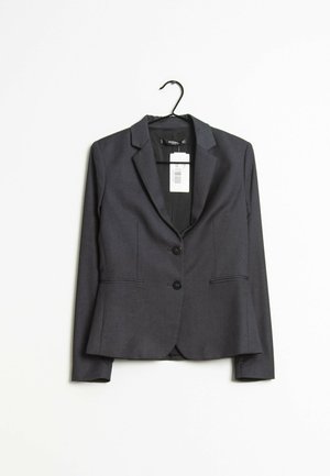 Blazer gris foncé cintré avec deux boutons et poches avant suspendu sur un cintre noir avec un fond blanc.