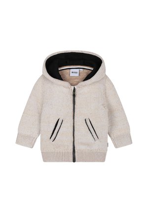 Hodie en tricot crème avec doublure noire, fermeture éclair à l'avant et deux poches latérales avec des accents de couture noirs.